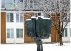 verschneites Denkmal auf dem Campus, dahinter C-Bau